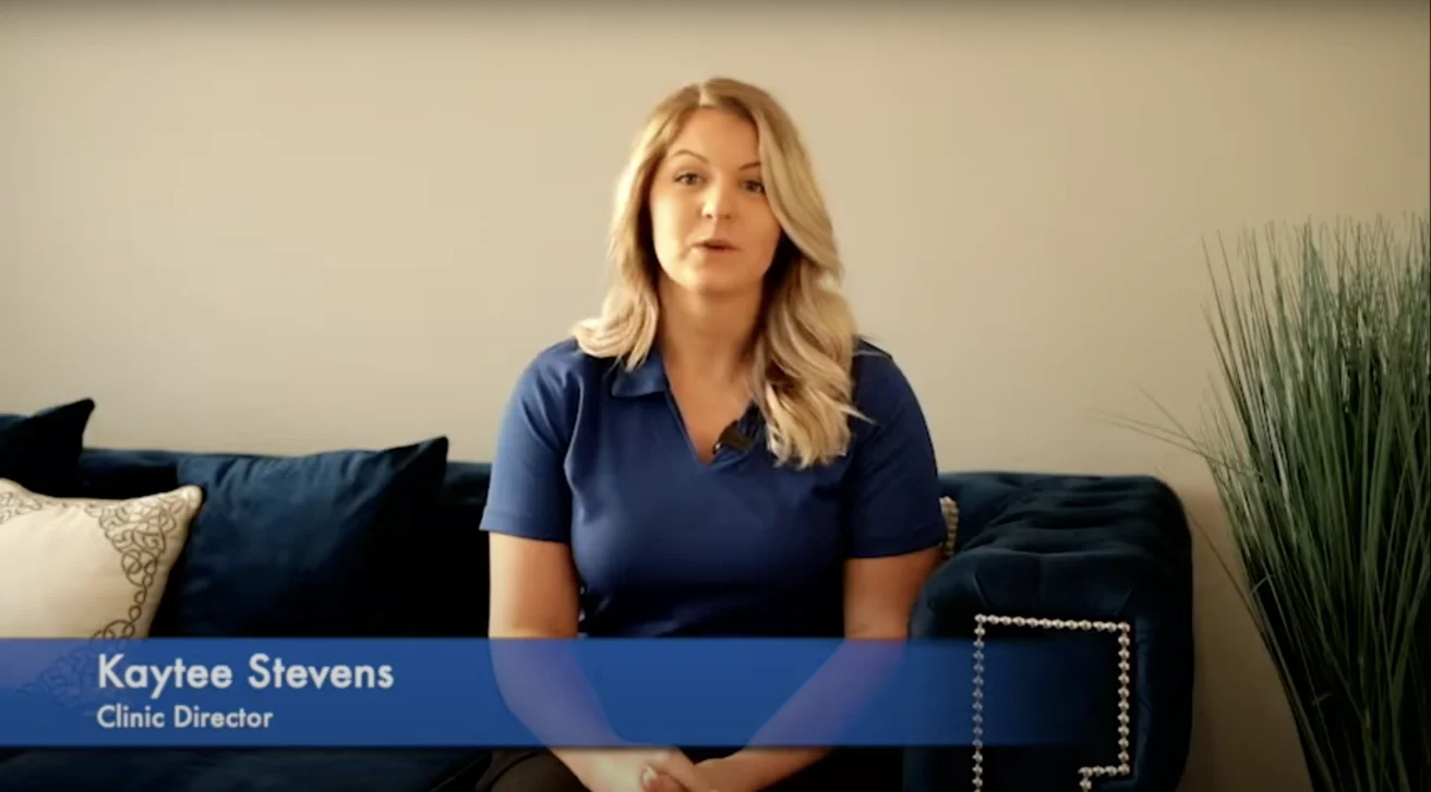 Woman in blue polo shirt sits on a blue sofa. The text reads "Kaytee Stevens, Clinic Director.